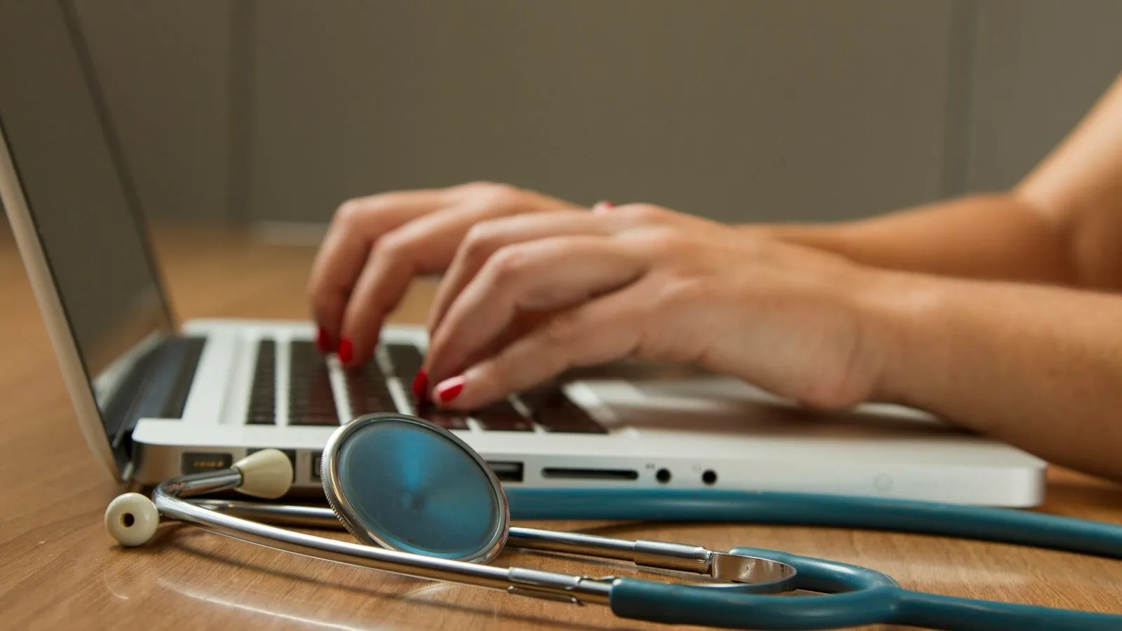 Clinician documenting on a laptop with a stethoscope on the desk