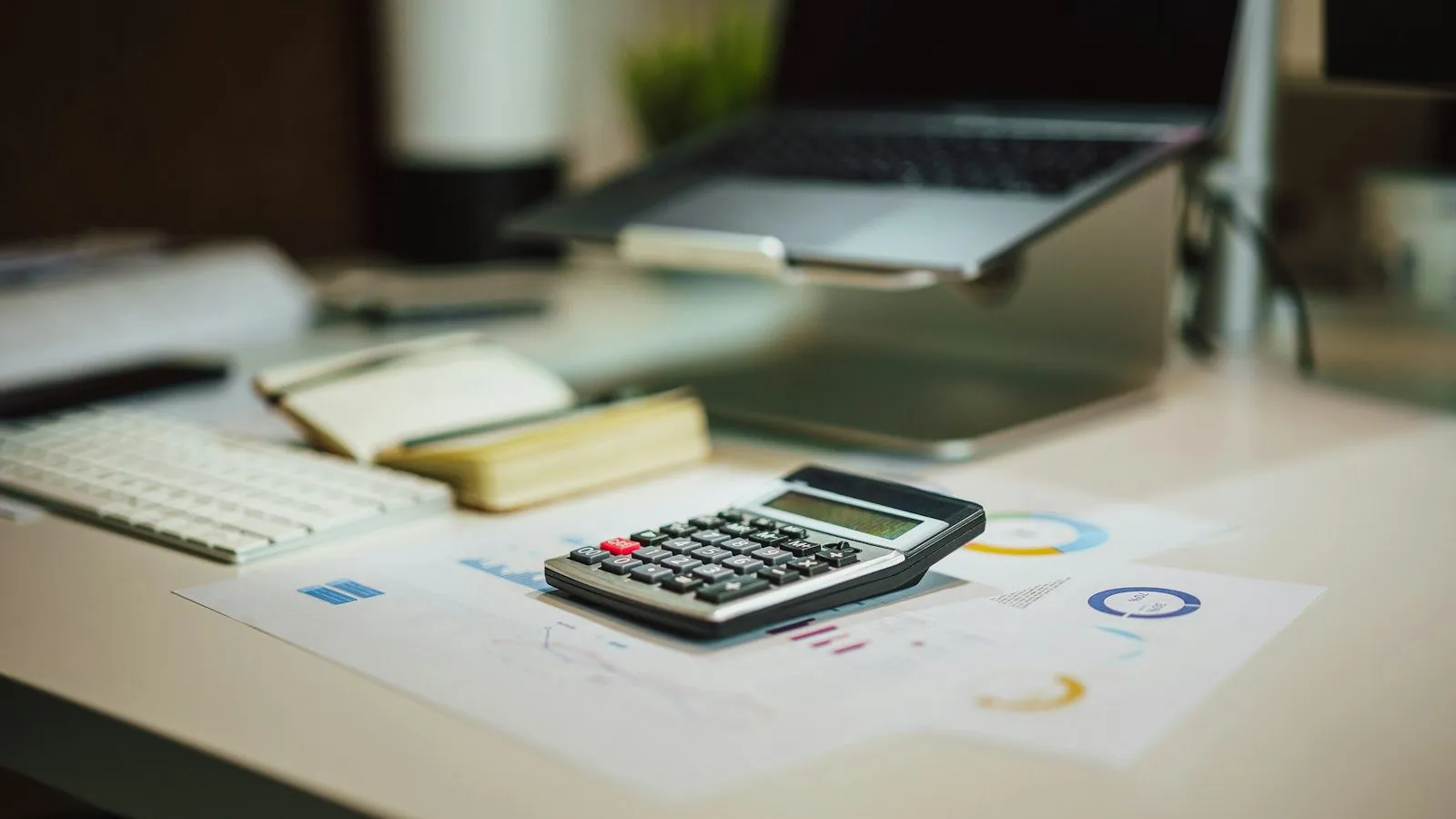 Calculator and printed charts on a desk beside a laptop, representing the cost of ADHD testing for clinicians