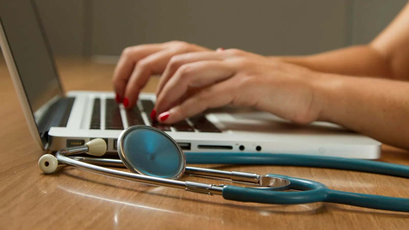 Clinician typing on a laptop next to a stethoscope while reviewing prescribing guidance