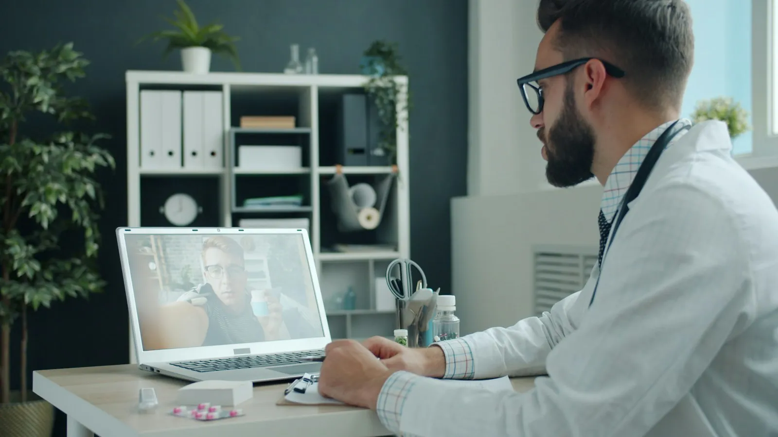Clinician holding a telehealth video visit with an adult patient on a laptop, reviewing medication